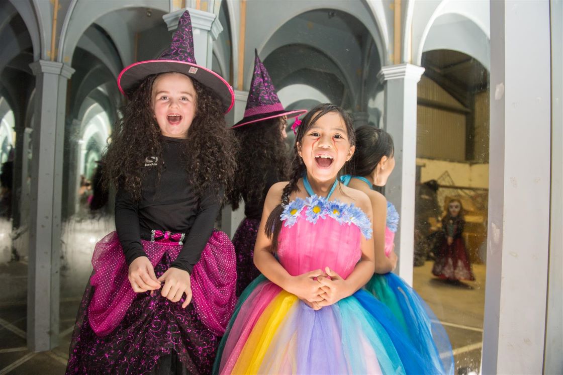 two girls in fancy dress costumes stand in front of a mirror screaming
