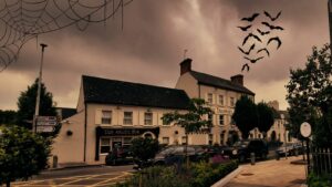 Photograph of the Headfort arms hotel with orange tint and a group of bats flying in the sky above.