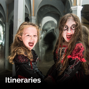 2 girls holding hands, dressed in red and black halloween costumes and screaming with the word 'Itineraries' overlayed on the bottom left of the picture