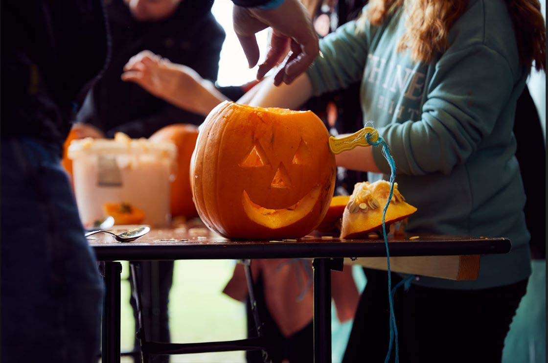 close up of people standing at a table carving a pumpkin
