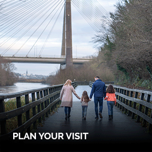 Photo of a family walking down a path with railings on either side of the path and a bridge in the distance